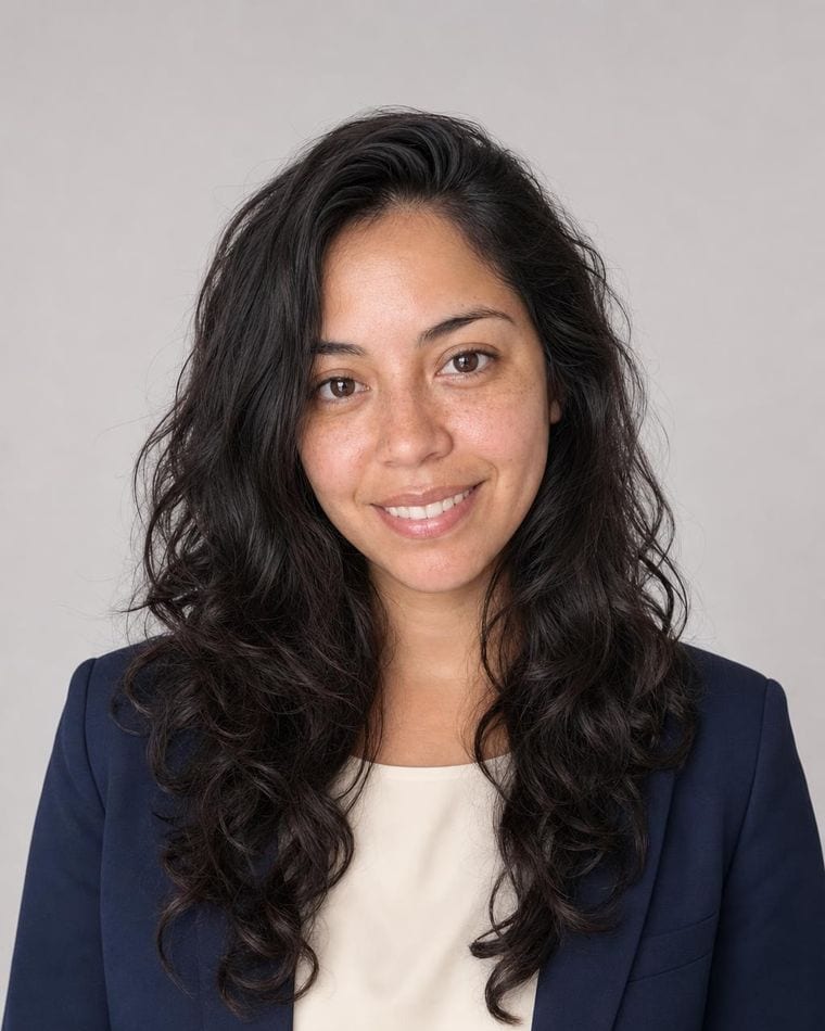 The same person as a finished studio headshot: navy blazer, ivory shell top, light grey backdrop.