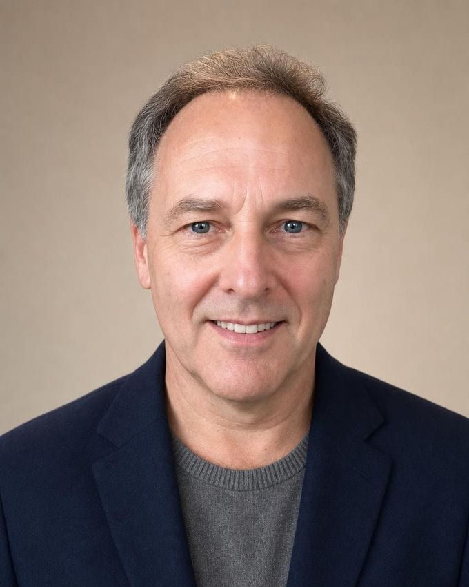 The Approachable: a man in a navy blazer over a grey knit against a warm greige backdrop, lit by soft window light.